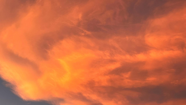 Wispy, wavy clouds like swirling milk, overhead and glowing gold, orange, and red, capturing the last light from the setting sun.