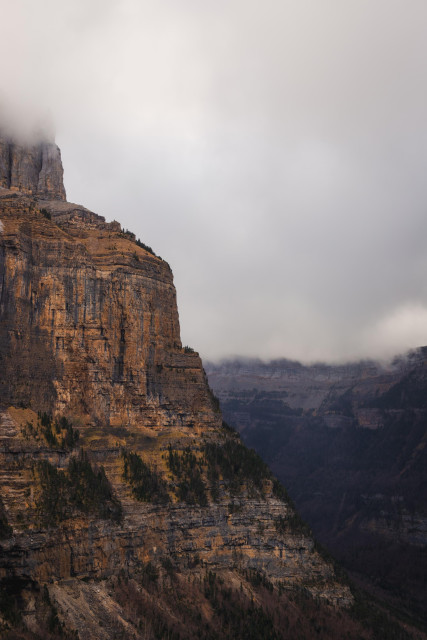 Fotografía vertical donde se ven amplias vistas de formaciones montañosas. Una pared de roca en la izquierdo que hace valle con una cordillera que se ve en el derecho y que forman la entrada al valle de Ordesa.