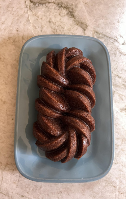 A shiny, dark brown loaf with an intricate Bundt pan pattern on a light blue oblong plate on a granite countertop 