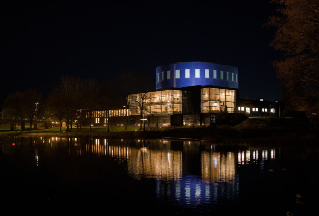 Ett upplyst Gävle konserthus, speglat i Gavleån.