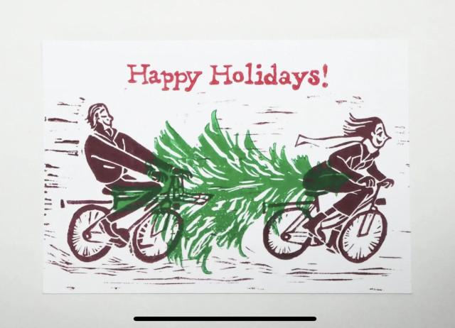 Hand-pressed holiday card, illustration of a woman and a man cycling while carrying a Christmas tree between their two bikes.