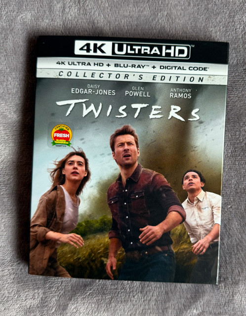 The 4K UHD Blu-ray of Twisters with three people staring frightened up at something between us and them. There is a scary twister behind them.  It sure what’s in front of them. 