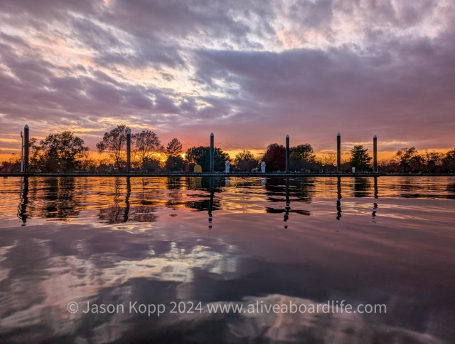 Edge of market dock and pilings reflect in still Washington Channel with pink clouds and orange and golden horizon