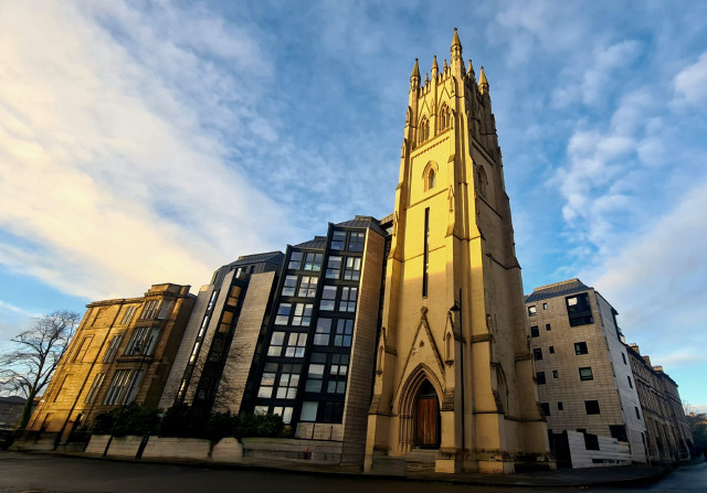 A Victorian Gothic church tower surrounded by modern buildings.