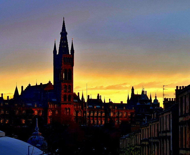 A sunrise behind an ornate, Gothic style university building.