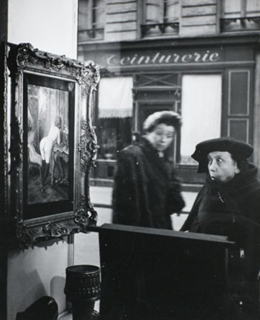 Photography. A black and white photo from a shop window shows two women standing in front of the window and looking at a painting. A laundry can be seen in the background. The two older women are wearing winter coats and hats and are visibly horrified by the framed painting hanging on the wall. It shows a naked woman getting into her bath (the simple painting was 50 years old and was by an unknown artist called Wagner).
Info: 
The photo appeared as the series "Le regard oblique" together with seven similar photos in the US magazine Life in May 1949. The shop window belonged to the antique store of Robert Miquel, who also worked as a reporter and was a friend of Robert Doisneau. The store was located at 15 Rue de Seine. The two noticed the astonishment and confusion of their compatriots when they saw the naked woman and decided to take a series of photographs. The photos are world-famous because they have been used for many purposes. This photo, for example, fetched a price of 9,500 US dollars at auction.