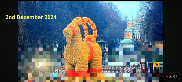 The Gävle Goat on the morning of 2nd of December 2024.

Picture shows a large straw effigy of a goat with red trimmings surrounded by a fence. Behind the goat a tree lined esplanade and the Gävle theatre are visible. Parts of the image are pixelated to obscure people passing by.

Picture from YouTube Live Feed. 