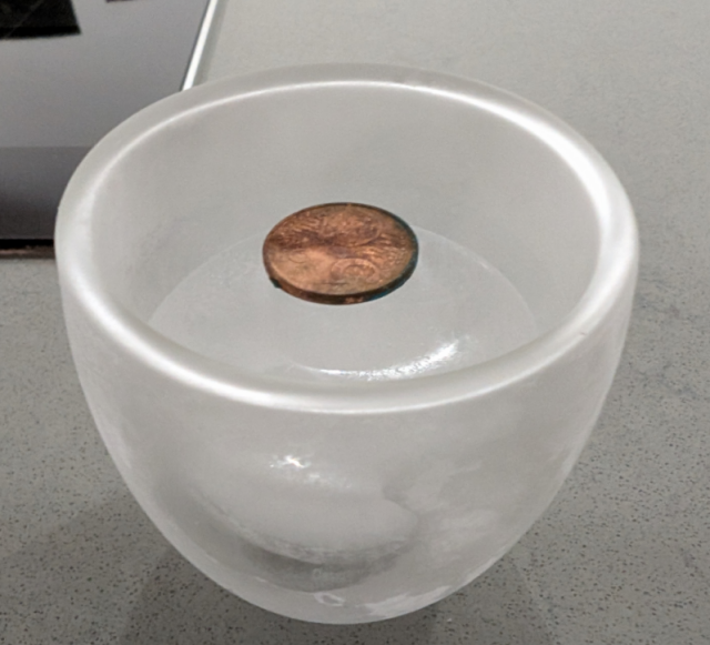 A frosty cup containing some ice, on top of which sits a penny.