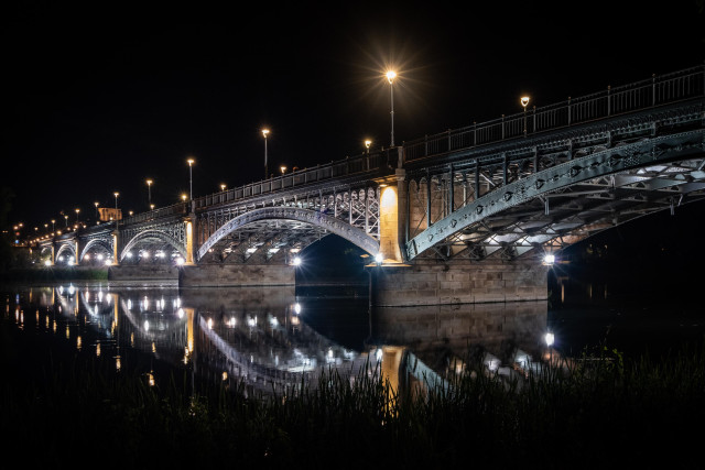 Fotografía nocturna donde se ve el puente Enrique Estevan de Salamanca reflejado en el río Tormes.