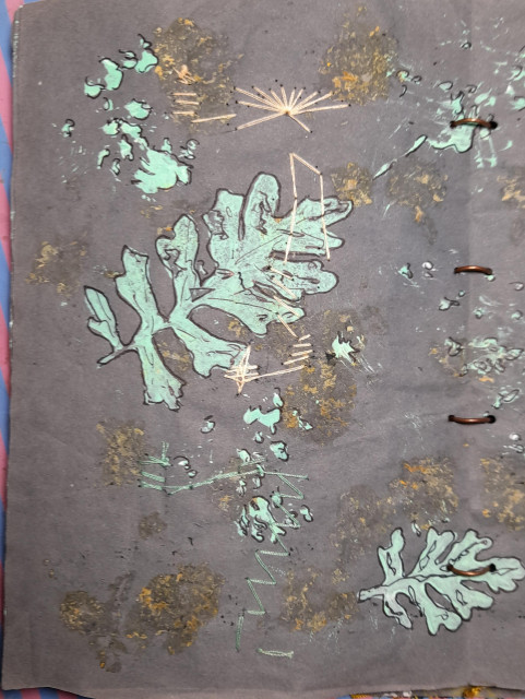 Back side of the embroidery: Bright green leaves imprinted on dark paper. The back side of the embroidery shows up on the dark paper and on parts of one leaf.