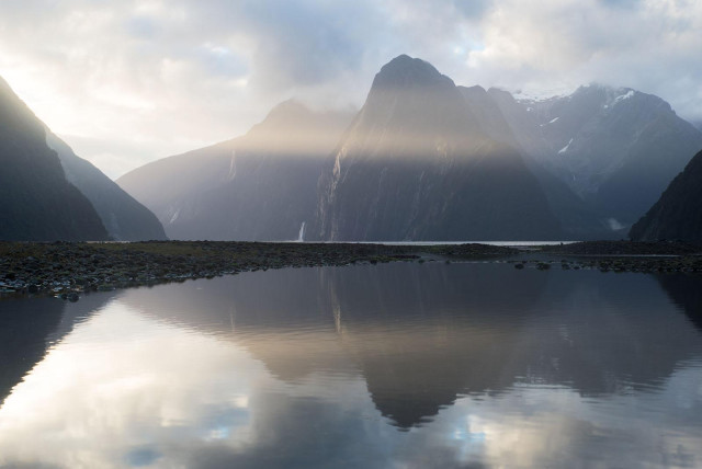 Milford Sound mountains reflecting in still waters with sunrays also reflecting