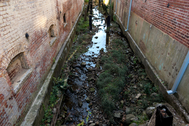 A stream running between two buildings, with supports from a former rail spur jutting upwards at various angles.