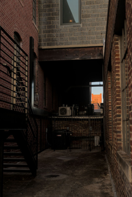 A gap between a skybridge, a rooftop below, and two buildings, framing a tower in the distance.