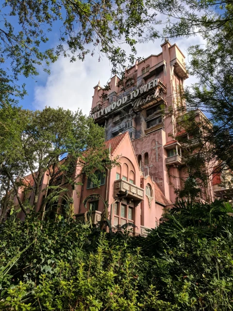 The Hollywood Tower "Tower of Terror" in Disney World, framed by green trees. A blue cloudy sky in the background.