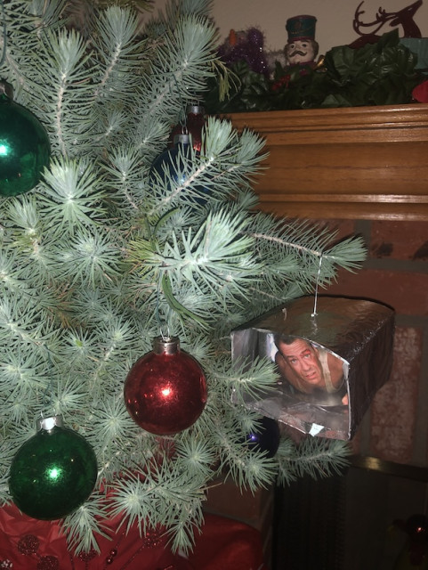 A close up of a Christmas tree with three glass bulbs and a silver ornament containing a scene from the holiday movie Die Hard.