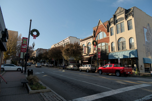 An urban street view from the corner of Craghead St. A row of parked cars sit in front of a solid block of buildings.