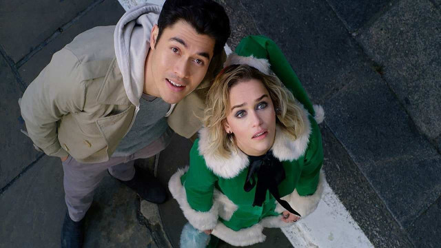 Henry Golding and Emilia Clarke (dressed like an elf) looking up. 