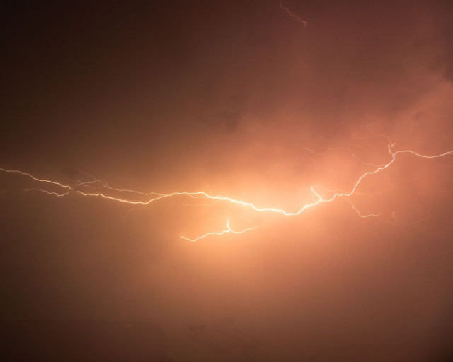 Ein horizontaler oranger Blitz vor einem bewölkten Nachthimmel.