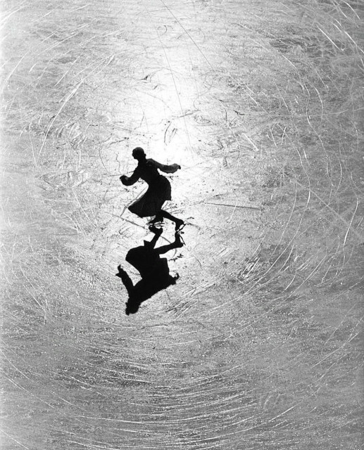 Photograph. An old black and white photo of a female ice skater on a frozen lake, taken from above. The sunlight falls like a spotlight on the young woman in the long dress in her athletic movement. She herself appears like a graceful shadow. All around her are the endless circles of scratched ice from her laps on the lake. Wonderful play with light and a perfect shot.
Info: The photograph shows the Austrian figure skating champion Melitta Brunner training on the ice in St. Moritz in 1934. Alfred Eisenstaedt (1898 - 1995) was one of the most influential photojournalists of the 20th century. He was adept at both humorous photo reportages and time-critical photographs. He photographed people from contemporary history as well as completely unknown people. Eisenstaedt preferred to rely on the lighting conditions he found and worked with highly sensitive film material and an open aperture; he did without flash and staged scenes in order to preserve the authenticity of the situation. (Wikipedia)