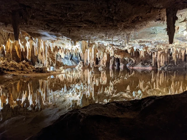 Photo taken inside a cave where there's standing water and the top of the cave is reflecting onto the water