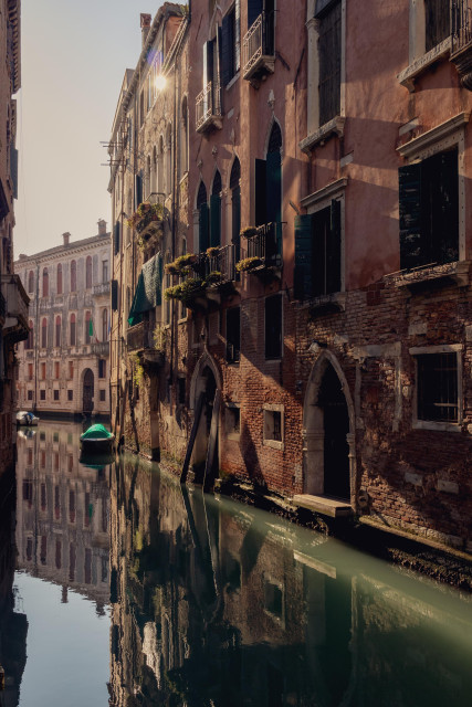 Fotografía vertical de parte de uno de los canales. En la parte derecha predomina una fachada donde hay reflejos de luz y sombra de la mañana.