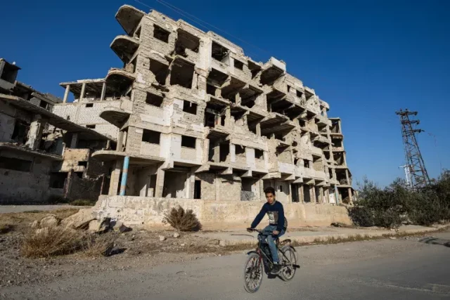 A Syrian boy rides his bicycle past destroyed buildings in the city of Harasta in Eastern Ghouta on the outskirts of Damascus [Sameer Al-Doumy/AFP]