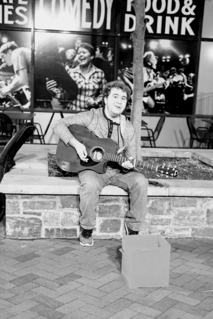 A man busking with a guitar in black and white