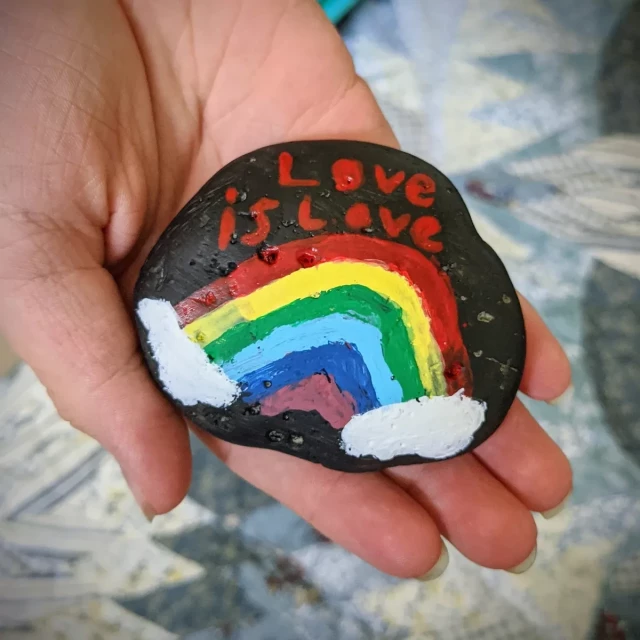 my daughter holding a small rock on which she painted a rainbow and the words "love is love"