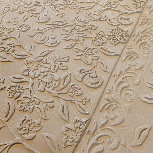 A closeup of a slab of clay rolled out and textured. The texture is cherries, cherry blossoms, and small branches with leaves. 