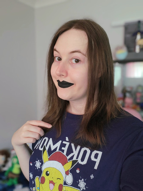 Selfie of Revy wearing black lipstick and a Pokemon Christmas shirt.
Her her is brown and mid length