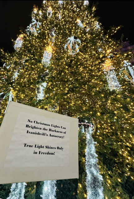 A sign placed next to the lit christmas tree outside parliament in Tbilisi, Georgia.
'No Christmas lights can brighten the darkness of Ivanishvili's autocracy! True light shines only in freedom!'