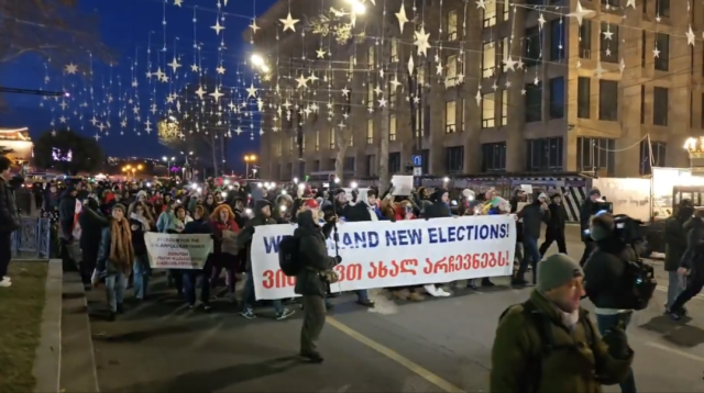 Election Observers march through the streets of Tbilisi under a huge banner that says "We demand new elections."