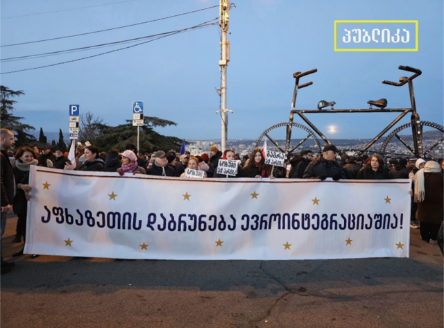 Protestors in Tbilisi Georgia stand behind a huge banner representing internally displaced people.