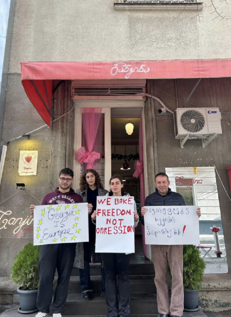 Staff stand outside a bakery in Tbilisi, Georgia with anti government signs. One says 'We bake freedom not oppression'