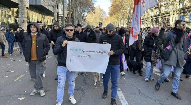 Protesting tech workers in Tbilisi Georgia hold up sign saying 'while government has bug we protest'