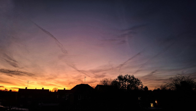 Bright gold sunrise on horizon with silhouette sky line of houses