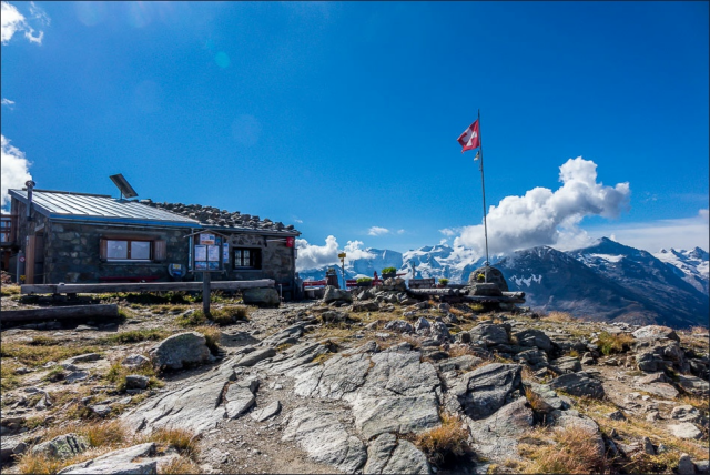 Segantini mountain hut on a rocky spot overlooking Swiss Alps. Swiss flag waving next to the hut. Blue skies.