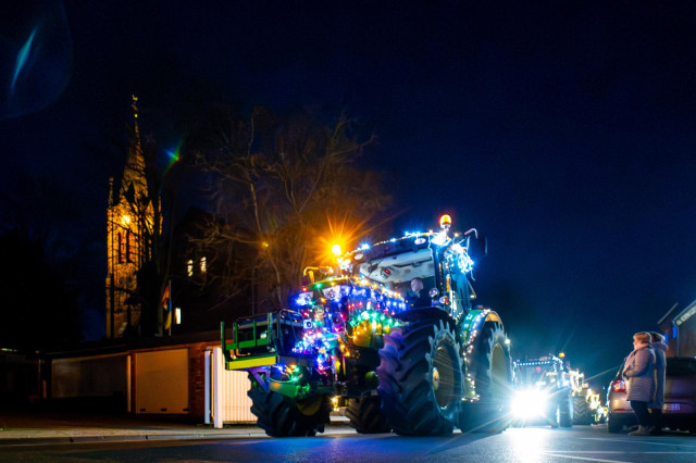 Ein mit vielen Lichtern behangene Traktor fährt durch unser Dorf. Im Hintergrund ist der beleuchtete Kirchturm zu sehen. 