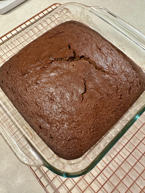 A gingerbread cake cooling in a glass 9x9 pan on a copper cooling rack on an off-white kitchen counter. No gingerbread men were transformed into magical talking creatures as a result of this picture or baking adventure. 