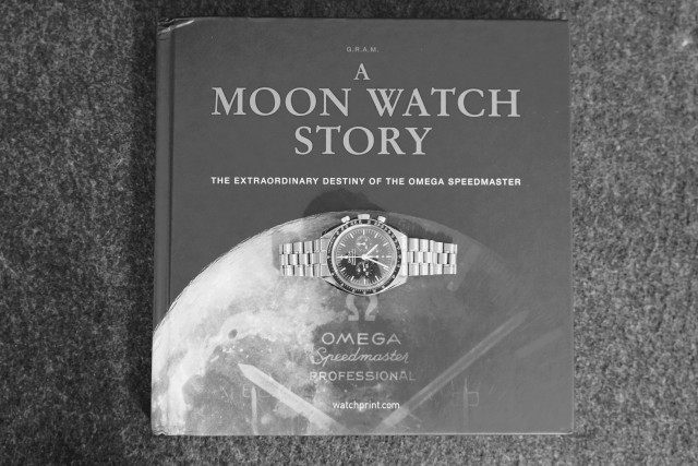 An Omega Speedmaster Professional sitting on top of the book A Moon Watch Stiry. 