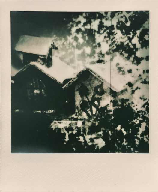 Double exposure Polaroid photo. Close up of tiny cardboard houses and a background of paint stains. Black and white.