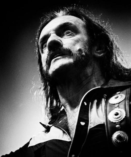 Black-and-white photograph of Motörhead frontman/bassist/vocalist Lemmy Kilmister. It is a portrait shot taken from below and slightly to Lemmy's left. He seems to be towering over the spectator, looking into the distance with an intense, almost crazed/maddened yet authoritive glare.