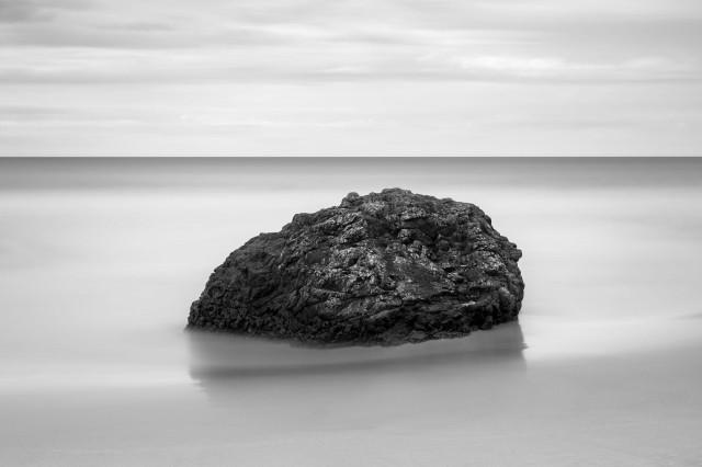 a minimalistic bw seascape with a black rock in the middle