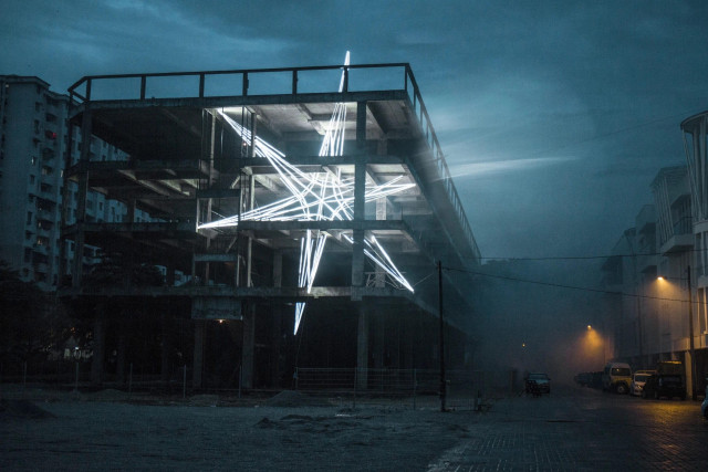 a monumental public art installation of a star shape made from LED strips inside of a concrete and steel building at night