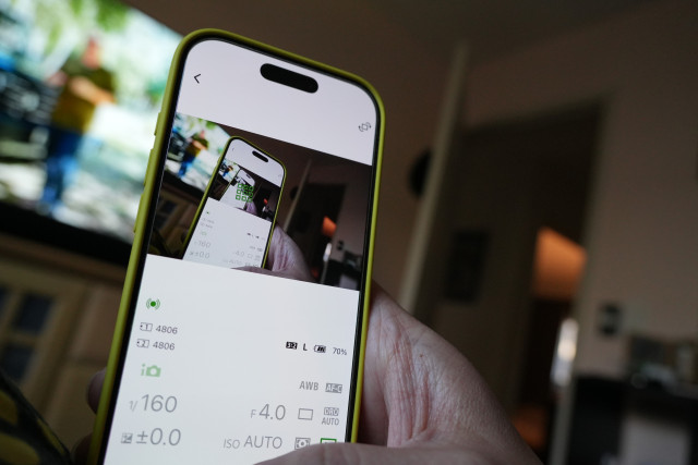 An iPhone 16 Pro running Sony Creators’ App remote controlling the camera shooting the picture of the iPhone 16 Pro running the Creators’ App. In the background a TV. 
