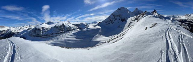 A panoramic view of snow-covered mountains under a clear blue sky, featuring a winding snow path and rugged peaks in the background. Part of a vision quest experience in the Canadian Rockies seeking growth. 