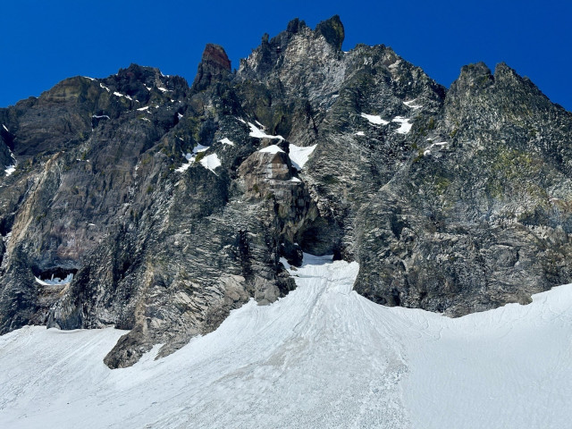 A rocky mountain face with steep, rugged cliffs and patches of snow against a bright blue sky. North face of Mt Thielsen, OR. 