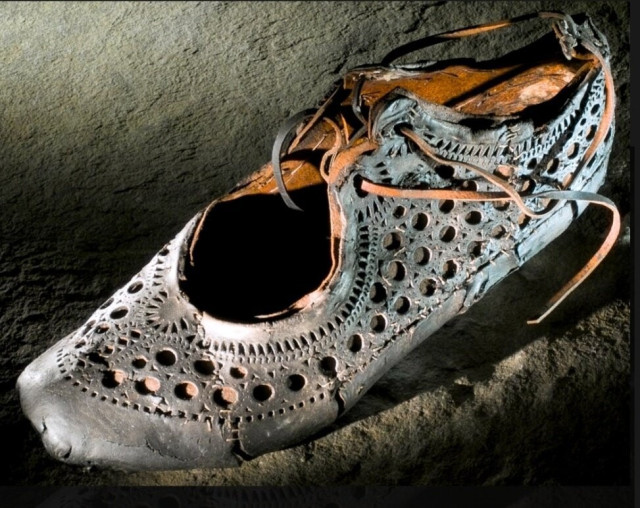 A close-up of a single leather shoe with a decorative pattern of holes of different sizes and shapes (e.g circles, triangles).