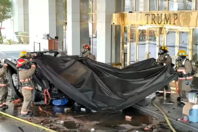 Firefighters in masks covering what looks like wreckage with a black tarp in front of a building with the letters TRUMP above its entrance.