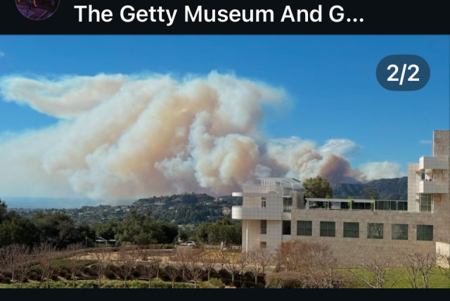 A large wild fire smoke and ash plume rising behind far away hills